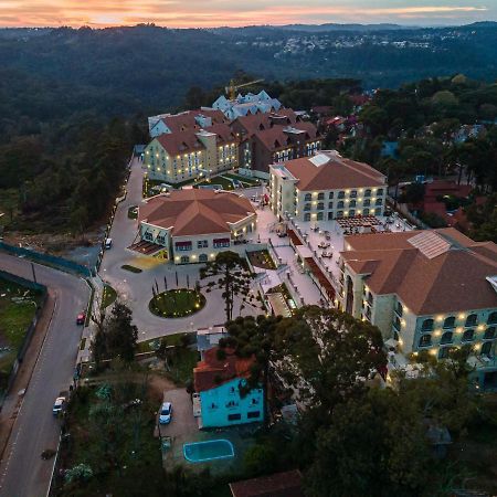 Buona Vitta Gramado Resort & Spa By Gramado Parks מראה חיצוני תמונה The photo shows an aerial view of a hotel complex set in a hilly, wooded area. The buildings feature a mix of architectural styles with several structures, including a central round pavilion. Surrounding the buildings are well-maintained gardens and 