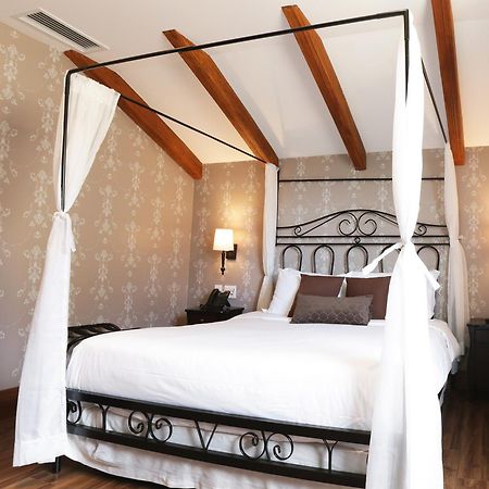 Buona Vitta Gramado Resort & Spa By Gramado Parks מראה חיצוני תמונה The photo shows a beautifully designed bedroom featuring a four-poster bed with a metal frame and flowing white curtains. The bed is adorned with white bedding and brown decorative pillows. The room has wooden beams on the ceiling and is decorated wi