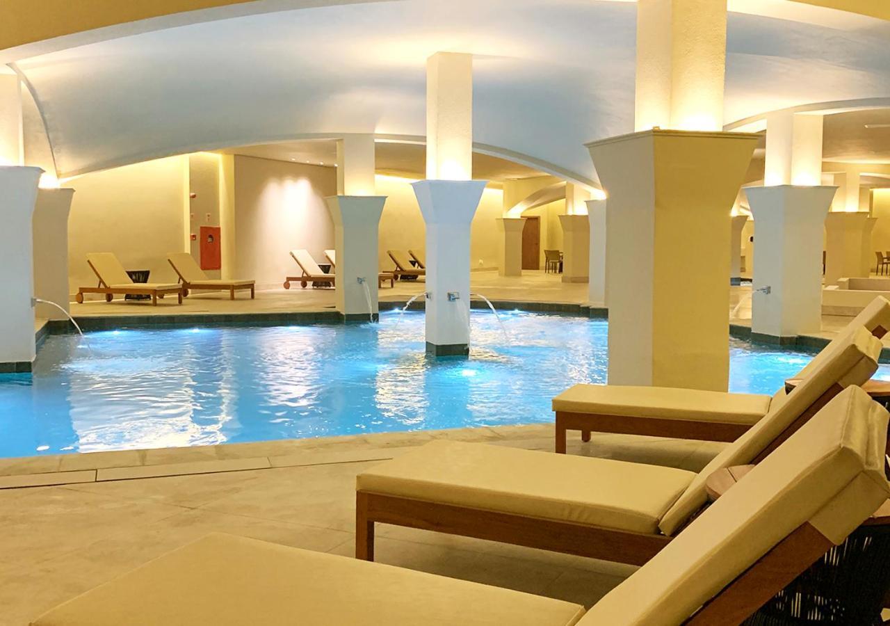 Buona Vitta Gramado Resort & Spa By Gramado Parks מראה חיצוני תמונה The photo shows an indoor spa or relaxation area with a tranquil atmosphere. There is a large swimming pool with clear blue water, illuminated by soft lighting. Surrounding the pool are several comfortable lounge chairs. The architecture features ele