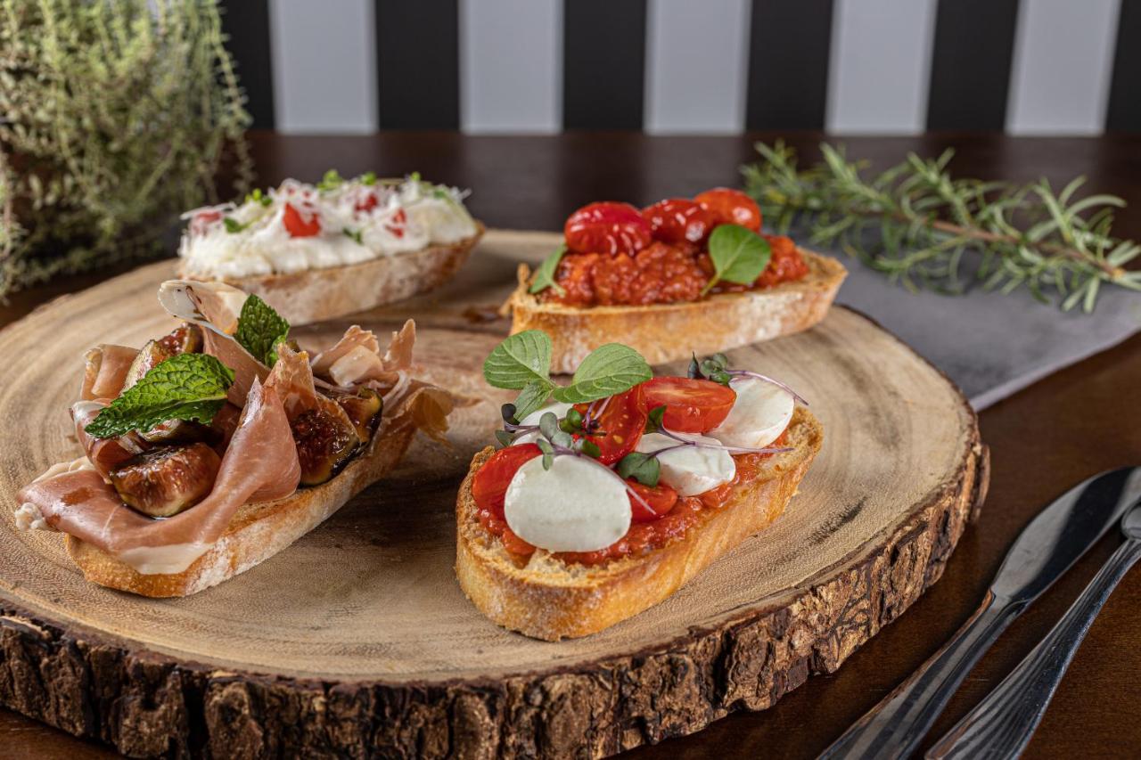 Buona Vitta Gramado Resort & Spa By Gramado Parks מראה חיצוני תמונה The photo displays a wooden serving platter featuring four different types of bruschetta. Each piece of bruschetta is topped with various ingredients:

1. The top left has a creamy spread, possibly cheese or ricotta, garnished with fresh herbs and sm