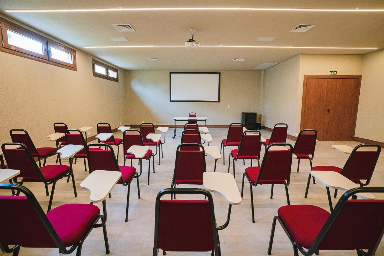 Buona Vitta Gramado Resort & Spa By Gramado Parks מראה חיצוני תמונה The photo shows a classroom or meeting room set up for a presentation or lecture. It features several rows of red chairs, each with a small writing surface attached. There is a blank screen mounted on the wall at the front of the room, likely for dis