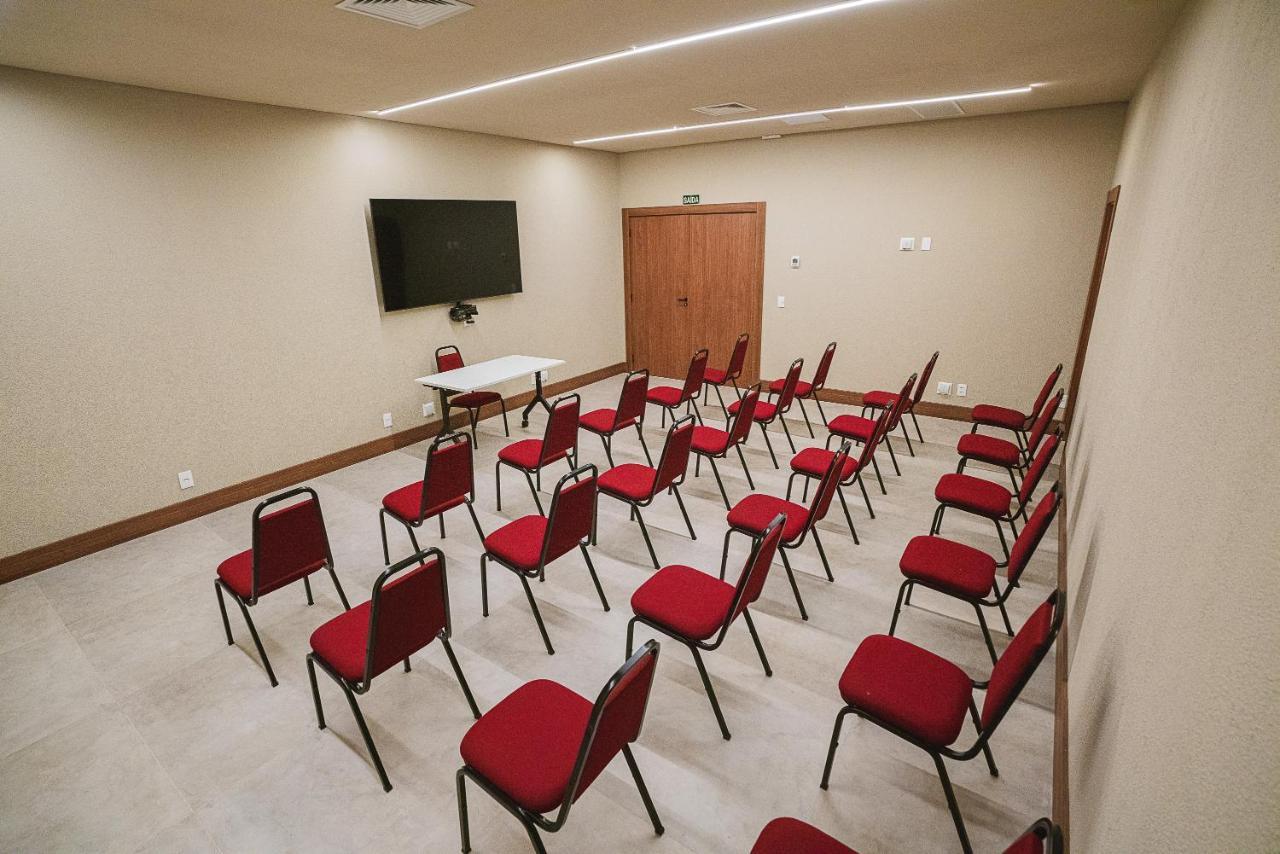 Buona Vitta Gramado Resort & Spa By Gramado Parks מראה חיצוני תמונה The photo shows a conference or meeting room with a simple and modern design. There are several rows of red chairs arranged in a semi-circle facing a white table at the front. On the wall opposite the chairs, there is a flat-screen television mounted