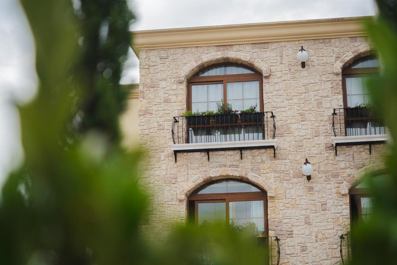 Buona Vitta Gramado Resort & Spa By Gramado Parks מראה חיצוני תמונה The photo depicts a stone building with a textured exterior. It features several windows with wooden frames. Each window has a small balcony adorned with decorative plants. There are also wall-mounted light fixtures flanking the windows. In the foreg