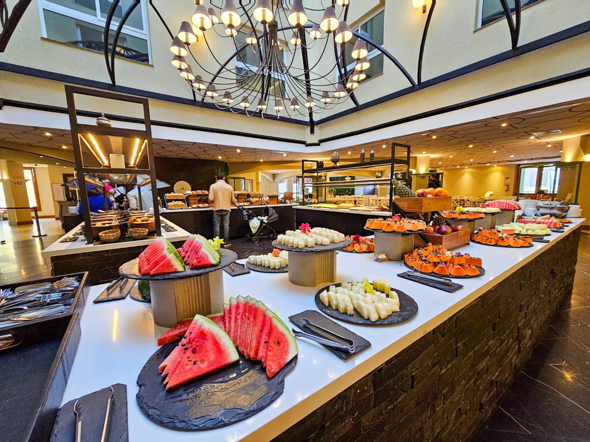 Buona Vitta Gramado Resort & Spa By Gramado Parks מראה חיצוני תמונה The photo depicts a lavish buffet setup in a dining area. In the foreground, there are several platters featuring an assortment of colorful food items, primarily fruits like watermelon and various types of sushi or rolls. The buffet table is elegantl
