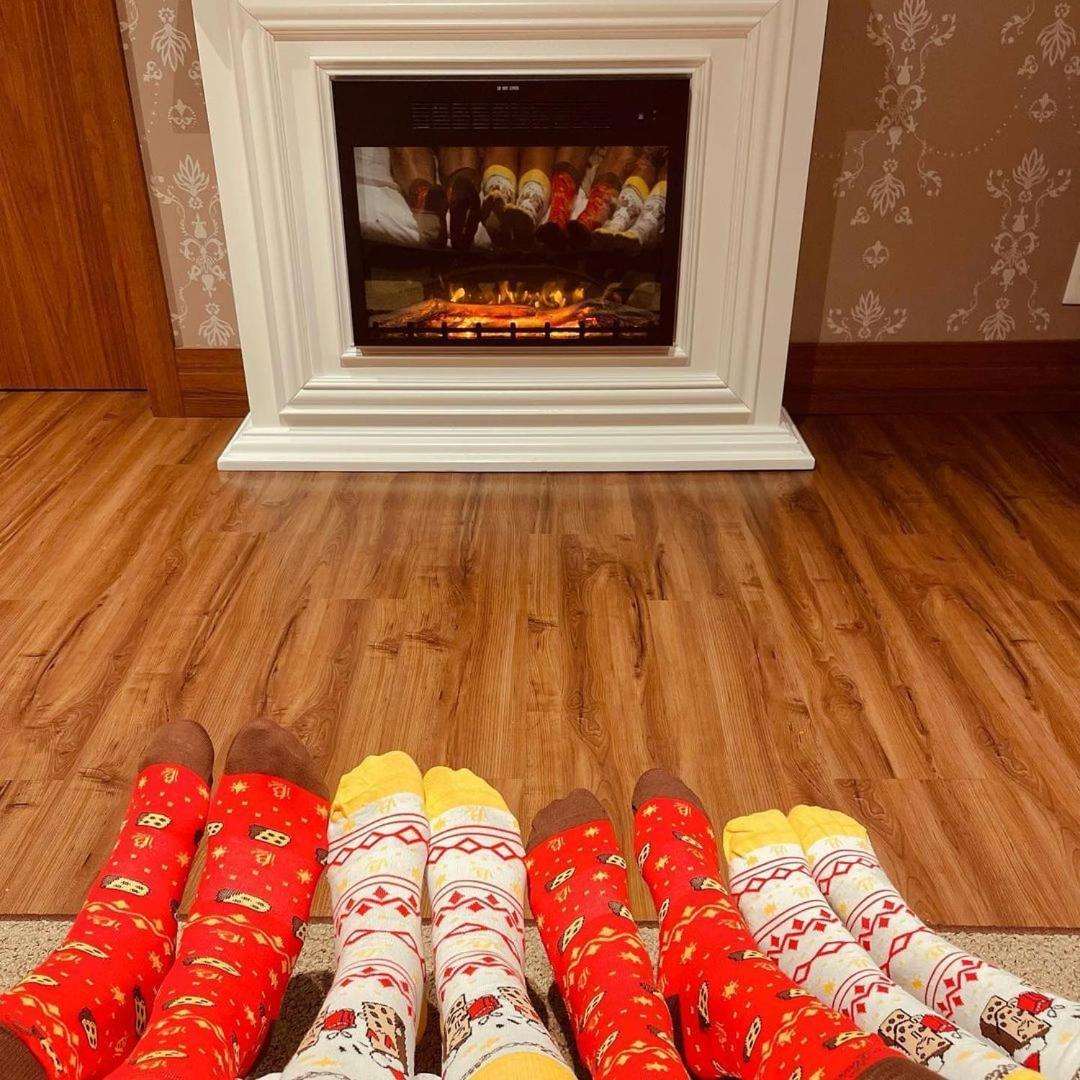 Buona Vitta Gramado Resort & Spa By Gramado Parks מראה חיצוני תמונה The photo shows a cozy indoor setting with a warm fireplace. In the foreground, several pairs of feet are displayed, each wearing brightly colored socks with various patterns. The socks include red, yellow, and white designs, contributing to a cheerf