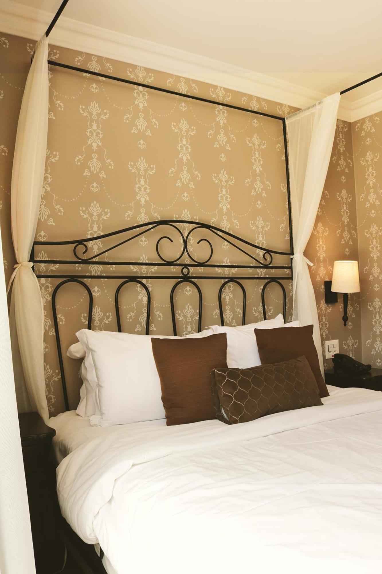 Buona Vitta Gramado Resort & Spa By Gramado Parks מראה חיצוני תמונה The photo shows a cozy bedroom setup featuring a decorative metal bed frame with a scroll design as the headboard. The bed is adorned with several white pillows and two brown decorative cushions. The wall behind the bed is covered with a light-colore