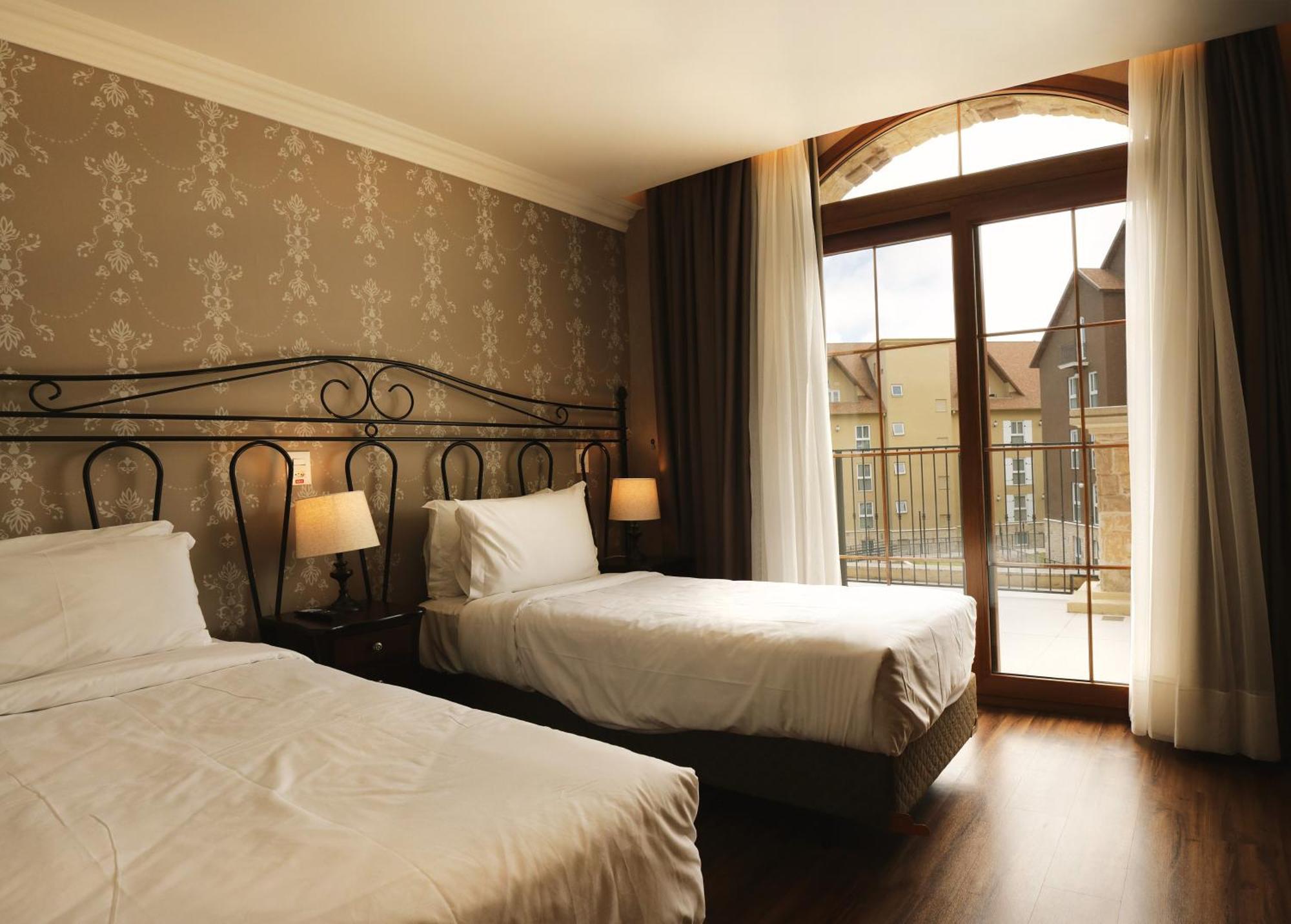 Buona Vitta Gramado Resort & Spa By Gramado Parks מראה חיצוני תמונה The photo shows a well-decorated hotel room featuring two beds. One bed is larger, likely a double bed, while the other is a single bed. The walls are adorned with a floral pattern, and there are bedside lamps next to the larger bed. Large windows wi