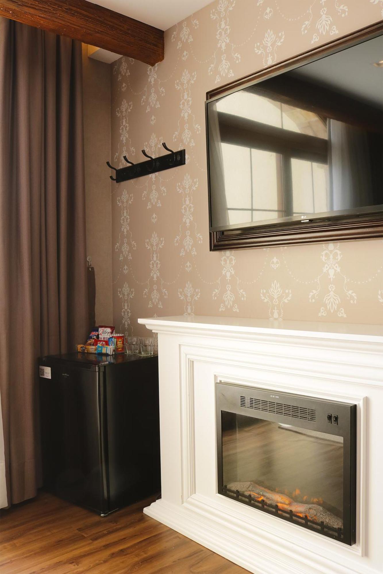Buona Vitta Gramado Resort & Spa By Gramado Parks מראה חיצוני תמונה The photo shows a room with a light-colored wall featuring a decorative pattern. On the right, there is a modern flat-screen television mounted on the wall. Below it, there is a white fireplace with a sleek design. To the left, there is a small black