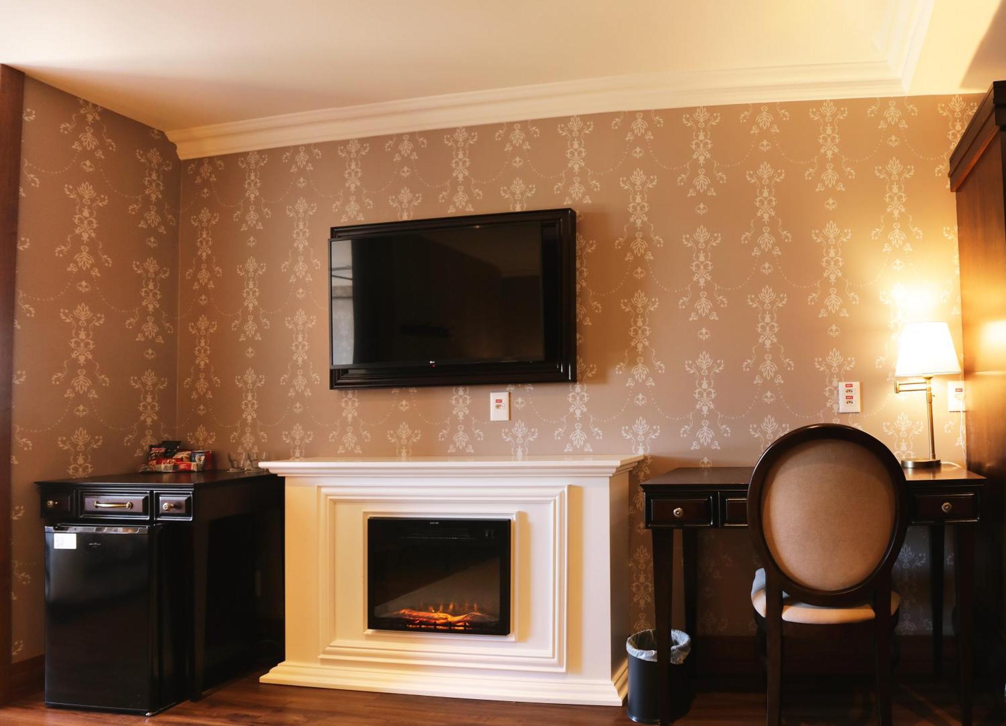 Buona Vitta Gramado Resort & Spa By Gramado Parks מראה חיצוני תמונה The photo shows a cozy room featuring a decorative wall with a subtle pattern. On one side, there is a modern flat-screen television mounted on the wall. Below it, there is a stylish electric fireplace framed in white. Adjacent to the fireplace is a 