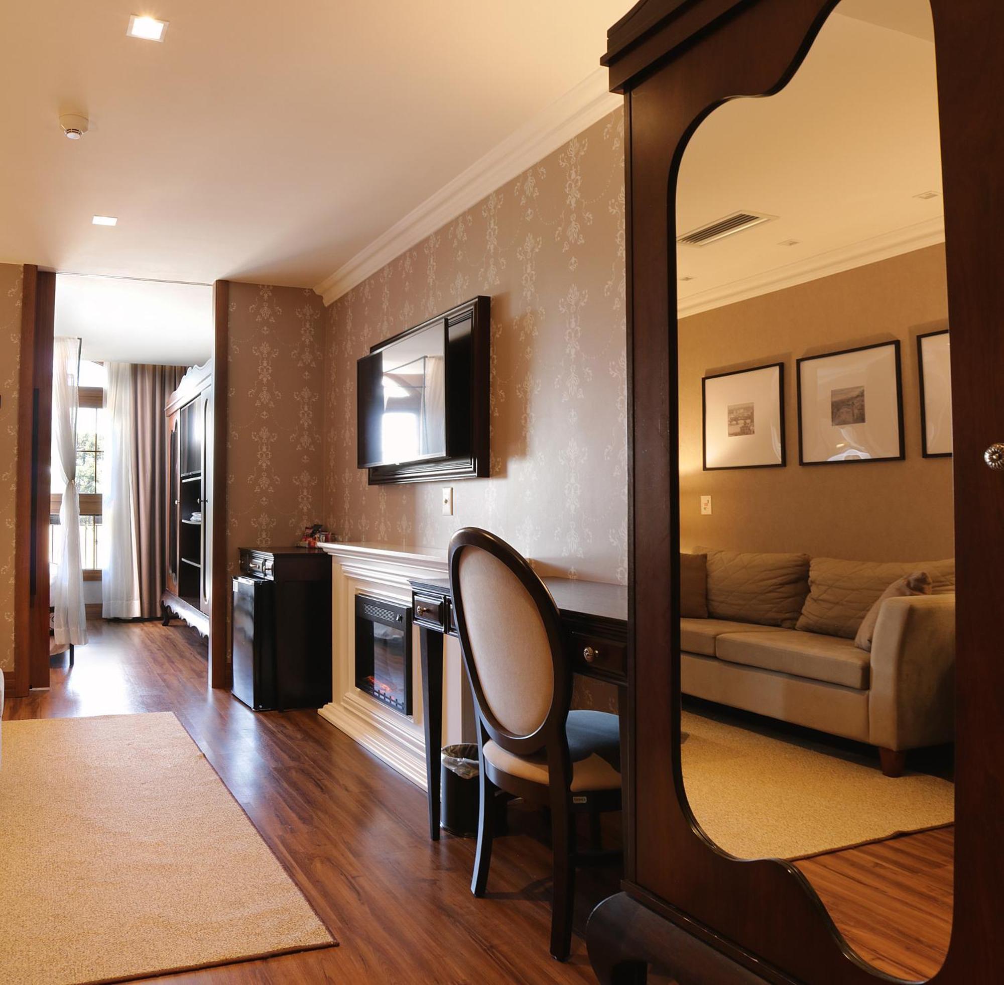 Buona Vitta Gramado Resort & Spa By Gramado Parks מראה חיצוני תמונה The photo shows a well-decorated room that appears to be a living area or a hotel suite. In the foreground, there is a round chair and a desk. A large mirror reflects the living space, creating a sense of spaciousness. 

On the wall is a flat-screen 