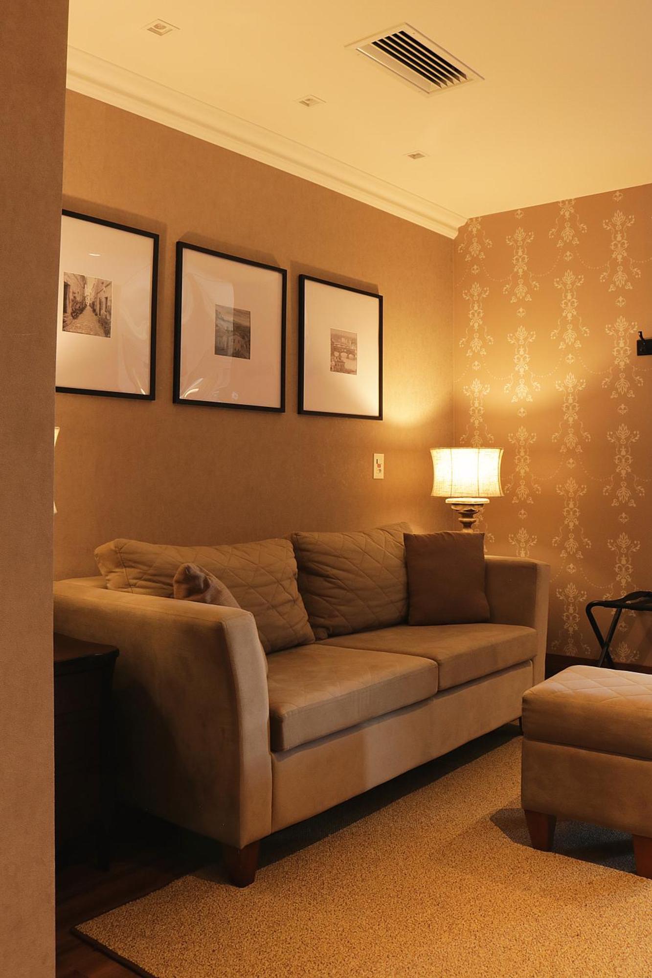 Buona Vitta Gramado Resort & Spa By Gramado Parks מראה חיצוני תמונה The photo shows a cozy living room setting. There is a light-colored sofa adorned with several cushions, positioned against a wall that has a subtle pattern. Above the sofa, there are three framed artworks or photographs hanging on the wall. To the s