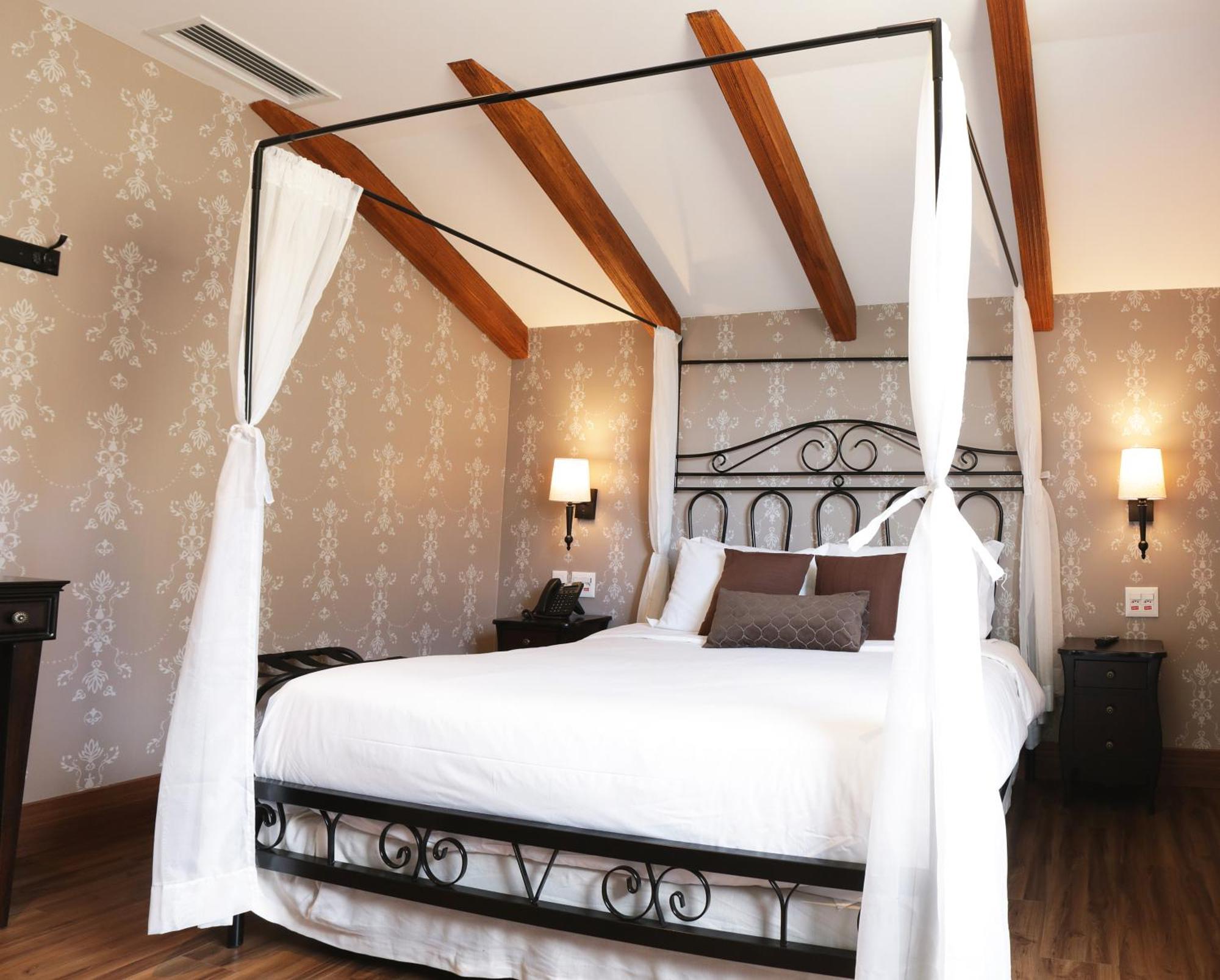 Buona Vitta Gramado Resort & Spa By Gramado Parks מראה חיצוני תמונה The photo shows a beautifully designed bedroom featuring a four-poster bed with a metal frame and flowing white curtains. The bed is adorned with white bedding and brown decorative pillows. The room has wooden beams on the ceiling and is decorated wi