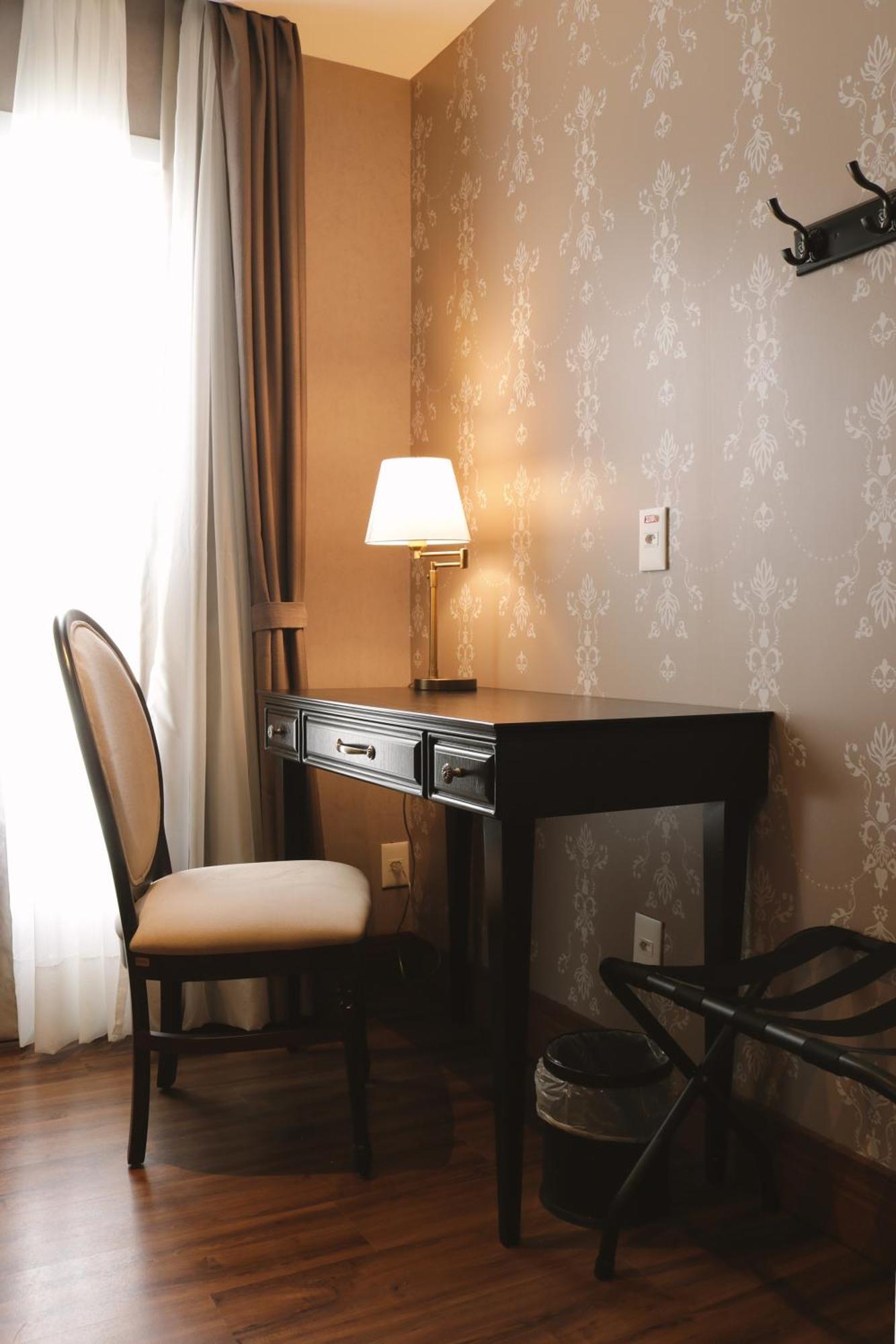 Buona Vitta Gramado Resort & Spa By Gramado Parks מראה חיצוני תמונה The photo shows a small desk set against a wall with a decorative pattern. The desk is black with a few drawers and has a small lamp on it. Next to the desk, there is a chair with a light-colored cushion. Soft light is coming through a window, castin