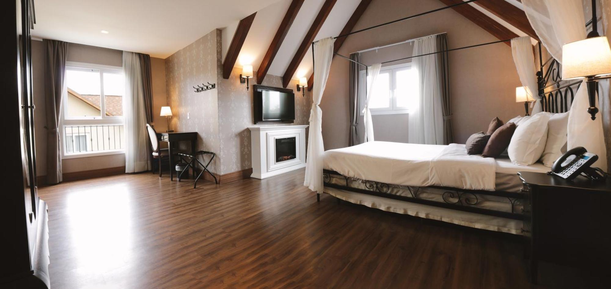 Buona Vitta Gramado Resort & Spa By Gramado Parks מראה חיצוני תמונה The photo shows a spacious hotel room with a modern and elegant design. There is a large bed with an overhead canopy, and the bed is dressed in white linens. To the side, there is a small seating area with a desk and chair. A flat-screen television i